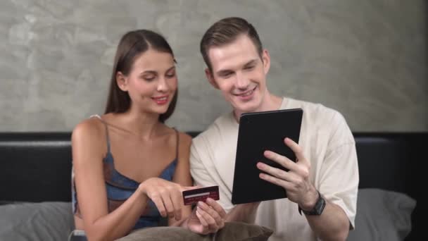 若いカップルは クレジットカードで支払うために オンライン決済アプリとデジタルウォレットを使用してホームベッドルームに座っています モバイルインターネットを介して商業ショッピングとモダンな購入 アディット — ストック動画