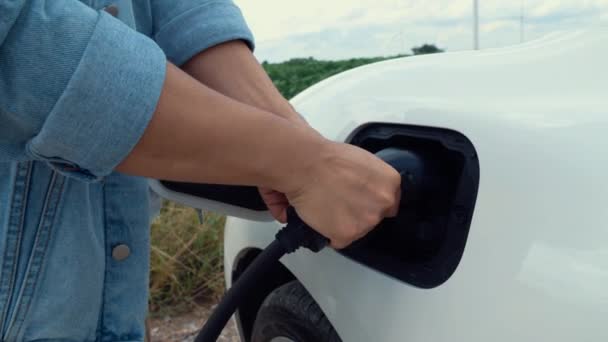 アジアの男は風力タービンによって動力を与えられる電気自動車にスマートEv充電器を挿入します 未来的なデジタルバッテリーステータスホログラムによる持続可能なクリーンEv技術のための再生可能エネルギー利用 パーセント — ストック動画