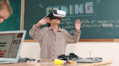 Kız kodlama sistemiyle uğraşırken metaworld 'e elektronik panoyla girmek için VR kulaklık takan bir çocuk. Çeşitli öğrencilerden oluşan bir grup program geliştirmek ve mühendislik kodu yazmak için birlikte çalışıyor. Pedagoji.
