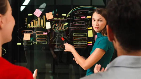 Executive manager pointing at business idea to present diverse investor team. Businesspeople listening female leader present marketing strategy while using sticky notes and mind mapping. Tracery