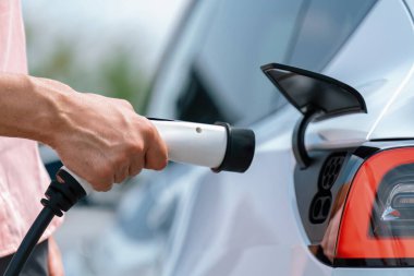 Dışarıdaki şarj istasyonundan EV şarj aletini şarj etmek için elektrikli araca elle tak. Alternatif temiz ve sürdürülebilir enerji kavramına sahip taze gün ışığı ortamı. Kalıcı
