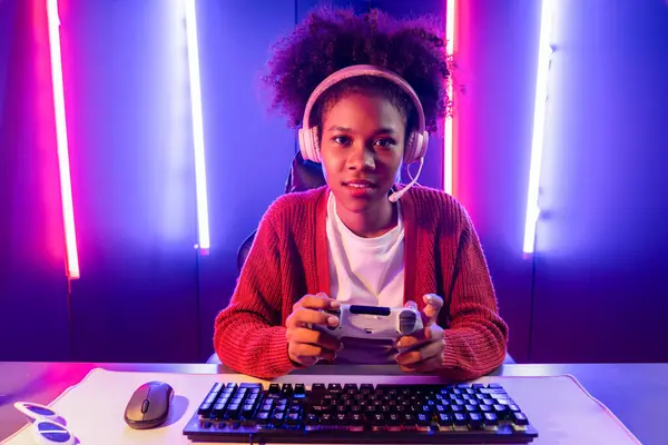 主办渠道的游戏流 非洲女孩玩在线游戏与操纵杆 与观众媒体在线话筒 在霓虹灯照明室里有熟练的团队队员 节衣店 — 图库照片