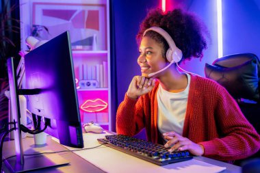 Neon renkli aydınlatma odasında kulaklık takan Afrika kökenli Amerikalı kız flamalı Esport yetenekli takımıyla online dövüş yapıyor. Rakiplerini kazanmak için strateji planlayan diğer oyuncularla konuşmak. Tatlandırıcı.