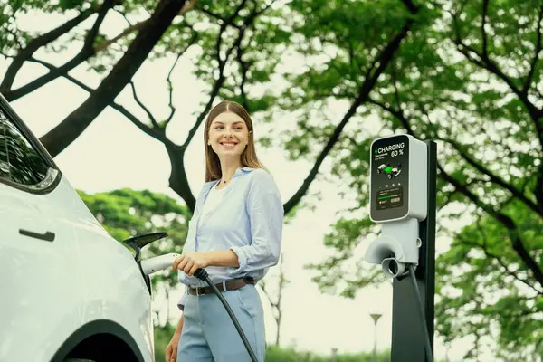 道路旅行中に電気自動車の電池を充電する若い女性 自然林や国立公園でEv車 休暇や休暇中にエコフレンドリーな旅行 エクスアルト — ストック写真