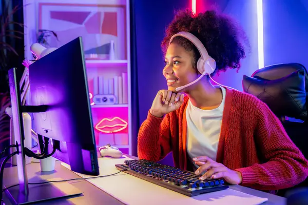Neon renkli aydınlatma odasında kulaklık takan Afrika kökenli Amerikalı kız flamalı Esport yetenekli takımıyla online dövüş yapıyor. Rakiplerini kazanmak için strateji planlayan diğer oyuncularla konuşmak. Tatlandırıcı.