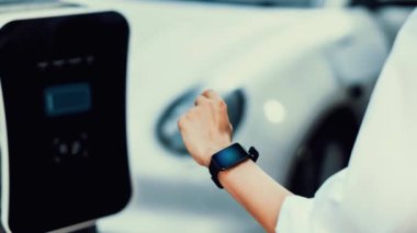 İş adamı, istasyonun otoparkından şarj olurken akıllı telefon hologramındaki EV aküsünün durumunu kontrol ediyor. EV teknolojisi adaptasyonu için temiz enerjinin gelecekteki yaşam tarzı. İnceleyin