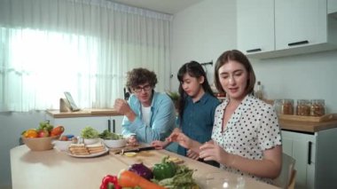 Baba, anne ve kız modern mutfakta salata pişirmek için birlikte zaman geçiriyorlar. Beyaz bir anne yemek tarifi ve yemek hazırlama hakkında açıklama yaparken aile sağlıklı bir kahvaltı hazırlıyor. Pedagoji.