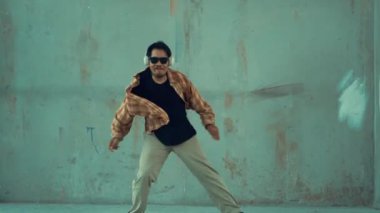 Çimento arka planında kulaklıktan müzik dinlerken sıradan sokak dansı yapan çekici İspanyol dansçı. Break dans gösterisinin hareketli çekimi. Açık hava sporu 2024 hiphop..
