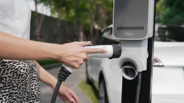 Genç bir kadın yazın yeşil sürdürülebilir şehir bahçesinde EV elektrikli arabasıyla seyahat ediyor. Kentsel sürdürülebilirlik yaşam tarzı yeşil temiz yeniden şarj edilebilir enerji elektrikli BEV araç iç organları