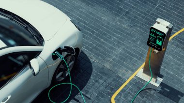 Şehir merkezindeki otoparktaki EV şarj istasyonundan hava görüntülü elektrikli araba şarj oluyor. Alternatif temiz ve sürdürülebilir enerji kullanan geleceğin yenilikçi yenilenebilir EV arabası. İnceleyin