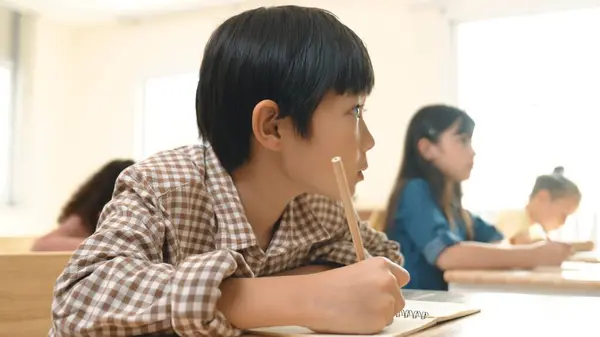 熟練したアジアの学生がテスト中に手紙を書いたり メモを取ったりします 小学生は 教室で授業や宿題をしている間 紙に取り組んでいます 教育コンセプト ペダゴロジー — ストック写真