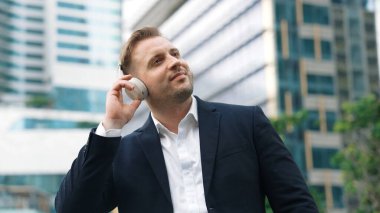 Erkek liderin etrafını sarın kulaklığı dinleyin ve neşeli ve motive edici bir şekilde rahatlatıcı müzikle dans edin. Becerikli proje yöneticisi şehir merkezinde akıllı telefon kullanırken rahat şarkılar dinlemeyi sever. Urbane.