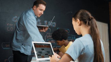 Afrikalı erkek manken tamir ederken beyaz kız programlama ya da kodlama sistemi. Öğretmen elinde dizüstü bilgisayar tutarken çeşitli çocukların web geliştirme programı yazmalarına bakıyor. Yenilik eğitimi. Öğretim.