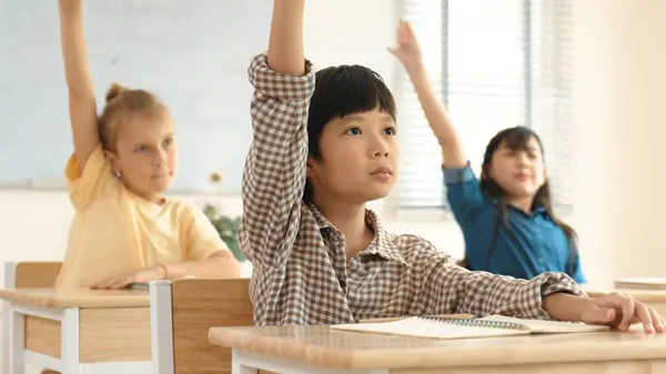 教室で勉強している多文化の子供たちに囲まれた先生に尋ね 答えるために手を挙げるスマートな少年 一緒に働く幸せな学生 ボランティア インストラクターを呼びます ペダゴロジー — ストック写真