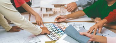 Yetenekli mimar takımı ev inşaatı hakkında tartışırken, iç mimar ev modeli ve bina planının dağıldığı renk paletine uygun bir renk belirliyor. Üst Manzara. Değiştirilmiş.