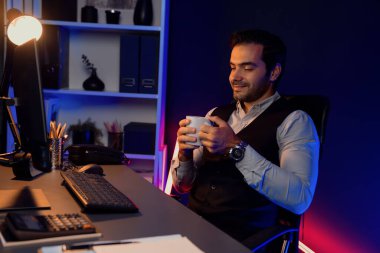 Gülümseyen zeki işadamı, elinde kahve fincanı olan satış ekibiyle buluşuyor ve geceleri Mor Neon Light Home Office 'deki bilgisayar ekranında ürün hedef pazarını araştırıyor. Tahmin et..