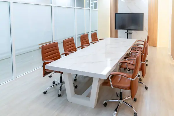 Modern meeting room interior with television for remote working. Modern white meeting table with chairs. Conference room surrounded by glass wall. No people. TV screen office background. Ornamented.