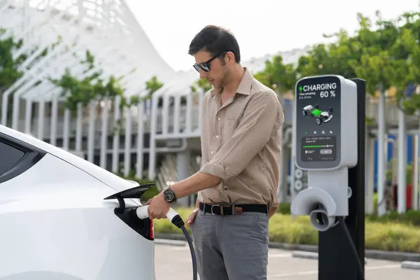 年轻人把电动汽车充电器从城市商业停车场的充电站充电给电动汽车充电 可再生能源电动汽车用于可持续环境友好型城市旅行 — 图库照片