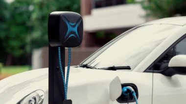 Elektrikli araba EV şarj kablosu ile şarj olmak için şarj istasyonuna bağlı. Geleceğin yenilikçi EV arabası ve enerji sürdürülebilirliği. Akıllı ve fütüristik ev enerjisi altyapısı. İnceleyin
