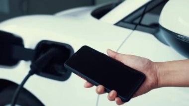 Akıllı telefon ekranı akıllı EV mobil uygulama üzerinde pil durumu EV araba garajdaki ev şarj istasyonu ile elektrik şarj ederken. Geleceğin yenilikçi EV arabası ve enerji sürdürülebilirliği. İnceleyin