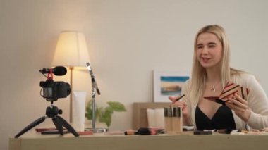 Sosyal medya için güzellik ve kozmetik video içeriği hazırlayan genç bir kadın. Güzellik blogcusu kamera ve ışık halkası kullanarak seyirciye ve takipçiye nasıl göz farı uygulanacağını gösteriyor. Blithe