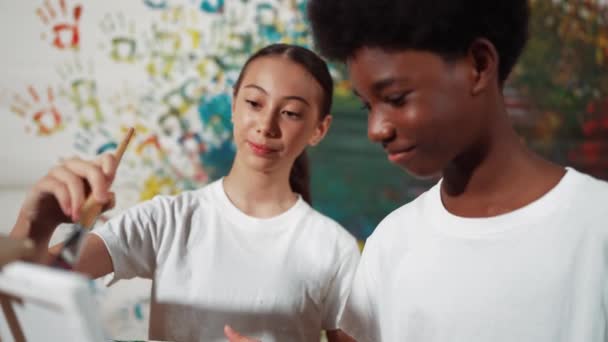 多姿多彩的孩子们把画布和色彩斑斓的墙壁一起画在一起 聪明的多文化学生穿着白衬衫在美术课上一起画画 创造性活动概念 — 图库视频影像