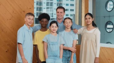 Mutlu öğretmen ve çeşitli öğrenciler kameraya gülümserken ayakta duruyorlar. Profesyonel akıllı eğitmen ve karışık ırk olan lise öğrencileri kameraya neşeli pozlar veriyor. Öğretim