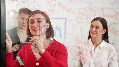 Başarılı proje yöneticisi fikrini cam tahtaya sunup yazarken aynı zamanda meslektaşına yaratıcı iş toplantılarında pazarlama stratejisini soruyor. Birlikte çalışmak, beyin fırtınası yapmak. Tertemiz..