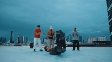 Profesyonel hippi hareketsiz poz verirken aynı zamanda şehir manzaralı çatıdaki müziğe ayak basıyor. Break dansçı, hip-hop dansçıları grubuyla birlikte sokak dansı yapıyor. Açık hava sporu 2024 hiphop..