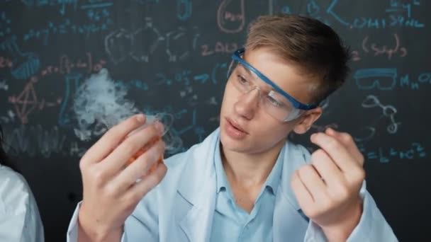 Zbliżenie Chłopca Sprawdzić Roztwór Chemiczny Trzymając Zlewkę Tablicy Teorii Chemicznej — Wideo stockowe
