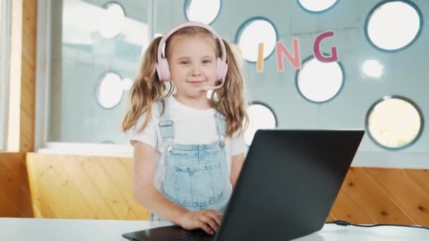 ラップトップを使用して働いたり ゲームをしたりする小さなかわいい少女 カメラを見ながら笑顔でコンピューターで作業する学生 子供はヘッドフォンを使用してオンラインクラスに参加します エラー — ストック動画