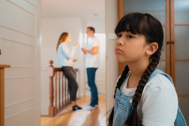 Stresli ve mutsuz genç kız arka planda ebeveynleri tartışırken köşede ağlayıp üzülüyor. Evde aile içi şiddet ve travmatik çocukluk depresyona dönüşür. Eşzamanlama
