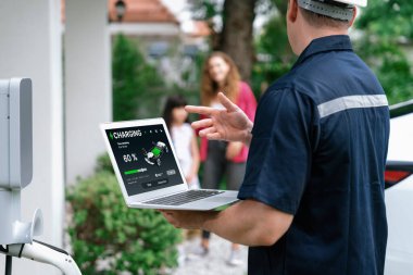 Evde EV şarj istasyonu kurulumu üzerinde çalışan nitelikli teknisyen, EV için dizüstü bilgisayarla şarj sisteminde sorun çıkarma ve yapılandırma ayarları yapıyor. Eşzamanlama