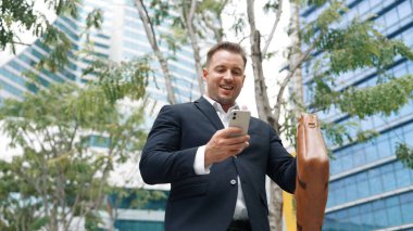 Şehir merkezindeki telefona bakan iş adamının düşük açılı kamera görüntüsü. Beyaz yöneticiler iyi haberler alırken aynı zamanda akıllı telefonlardan başlangıç projesindeki yatırımları ya da terfi almayı kontrol ediyorlar. Urbane.
