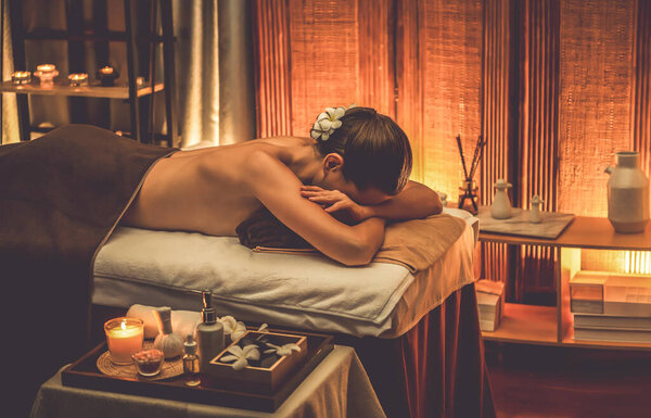 Caucasian woman customer enjoying relaxing anti-stress spa massage and pampering with beauty skin recreation leisure in warm candle lighting ambient salon spa at luxury resort or hotel. Quiescent