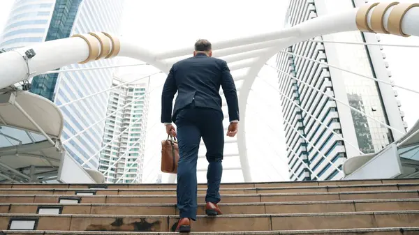 Smart caucasian businessman walking up stairs surrounded by urban view. Back view of ambitious project manager finding challenging job or investment opportunity at city with modern building. Urbane.