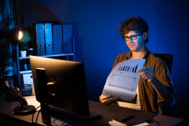 Genç işadamı, Neon Light Modern Ofis 'teki yeni proje surround çalışma masası için kağıt üzerinde tasarım düşünüyor. E-posta ile hediye göndermeden önce not defterine yeni bir iş düşünüyorum. Toplayıcı.