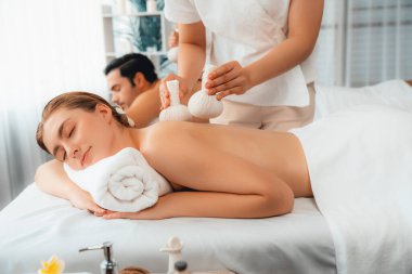 Sıcak bitkisel top spa masaj vücut tedavisi, masör nazikçe bitki torbasını çift müşteri vücuduna bastırıyor. Aromaterapi dinlenme sükuneti ve sükuneti kaplıca salonundaki atmosferi aydınlatıyor. Sessiz.