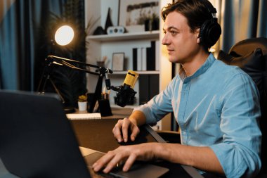 Sunucu kanalı akıllı yayıncı laptopta canlı sosyal medya uygulaması arıyor, kulaklık takıyor ve modern ofis stüdyosundaki mikrofonu kullanıyor. Bireysel.