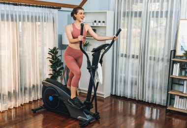 Spor ve atletik bir kadın, evdeki fiziğe ve sağlıklı spor yaşam tarzına uygun vücut egzersizi sırasında eliptik koşu makinesiyle koşuyor. Gaiety evde egzersiz eğitimi.