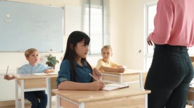 Asyalı mutlu öğrenci ilköğretim sınıfında soruları cevaplamak için gönüllü olurken öğretmen tahtaya cevap yazmak için öğrenciyi seçiyor. Sınıfta çeşitli çocuklar var. Pedagoji.