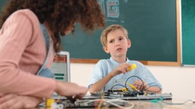 Beyaz tenli enerjik çocuk ana tahtayı tamir ediyor ve kameraya bakıyor. Bu sırada Amerikalı öğrenci de bilgisayar ekranı kodlu renkli kablolar kullanarak elektronik makineyi incelemek için birlikte çalışıyor. Pedagoji.