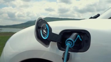 Elektrikli araba şarj istasyonuna bağlanır, EV şarj kablosu ile pili şarj edilir doğası gereği akıllı dijital batarya durum hologramı görüntülenir. Geleceğin yeşil enerji altyapısı. İnceleyin