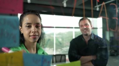 Profesyonel iş adamları yaratıcı pazarlama fikrini modern ofiste tartışırlar. İş adamları cam tahtada yapışkan notlar kullanarak finansal plan üzerinde çalışıyor. Yönlendirici.