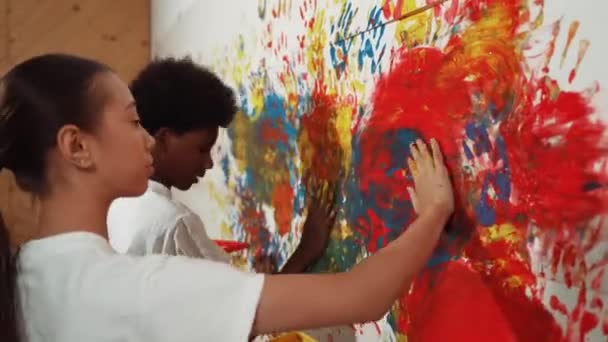 女孩和非洲男孩的侧面视图把手放在水彩画上 并在墙上贴上邮票 多元文化的孩子在艺术课上用生动活泼的手印画出色彩或装饰房间 — 图库视频影像