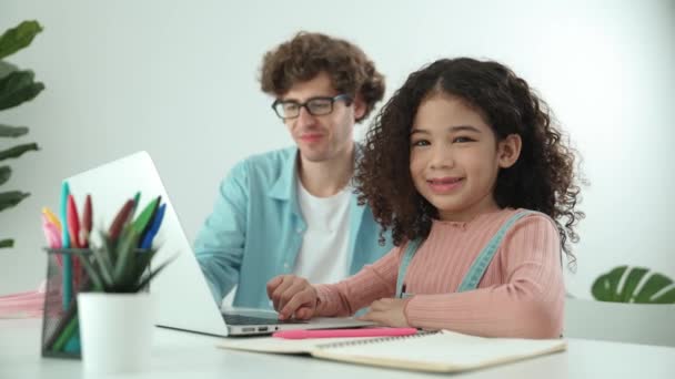 父親とラップトップで作業しながらカメラを見ているアメリカの学生は エンジニアリングコードをチェックするためにラップトップ画面を見ています ハッピースクールの女の子が笑顔で 放映の勉強をしている ペダゴロジー — ストック動画