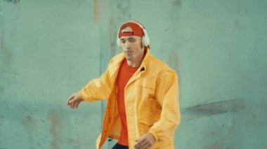 Beyaz hipster sokak, şehir merkezinde ayak sesleri gösteriyor ya da pratik yapıyor. Break dansçı, kulaklıktan müzik dinlerken hip-hop müziğine adım atıyor. Açık hava sporu 2024. Gri arka plan. hiphop.