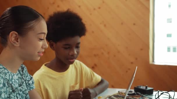 在Stem技术课上 穿着休闲布的非洲男孩和高加索女孩的现场视图与笔记本电脑和电子设备一起工作在桌旁编码提示或编程系统 — 图库视频影像