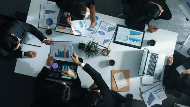 Toplantı odasındaki tabletten finansal istatistiklere bakan akıllı yöneticinin en üst görüntüsü. Masadaki yatırım verilerini not defteriyle analiz etmek için birlikte çalışan bir grup iş adamı. Müdürlük.
