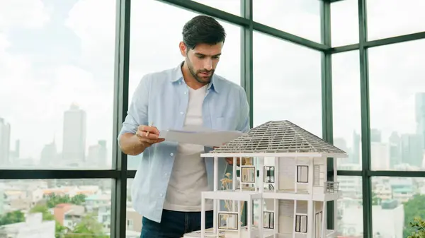 Professional architect engineer comparing between blueprint house model. Businessman decide to invested money in real estate project. Project manager checks house by comparing with plan. Tracery